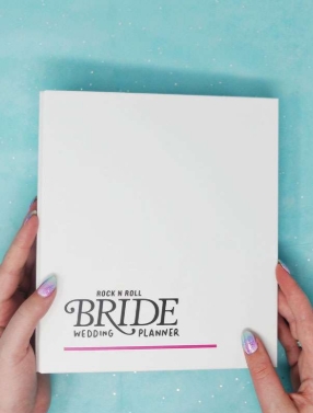 Bride researching online wedding planning resources on laptop with wedding inspiration and planning notebook